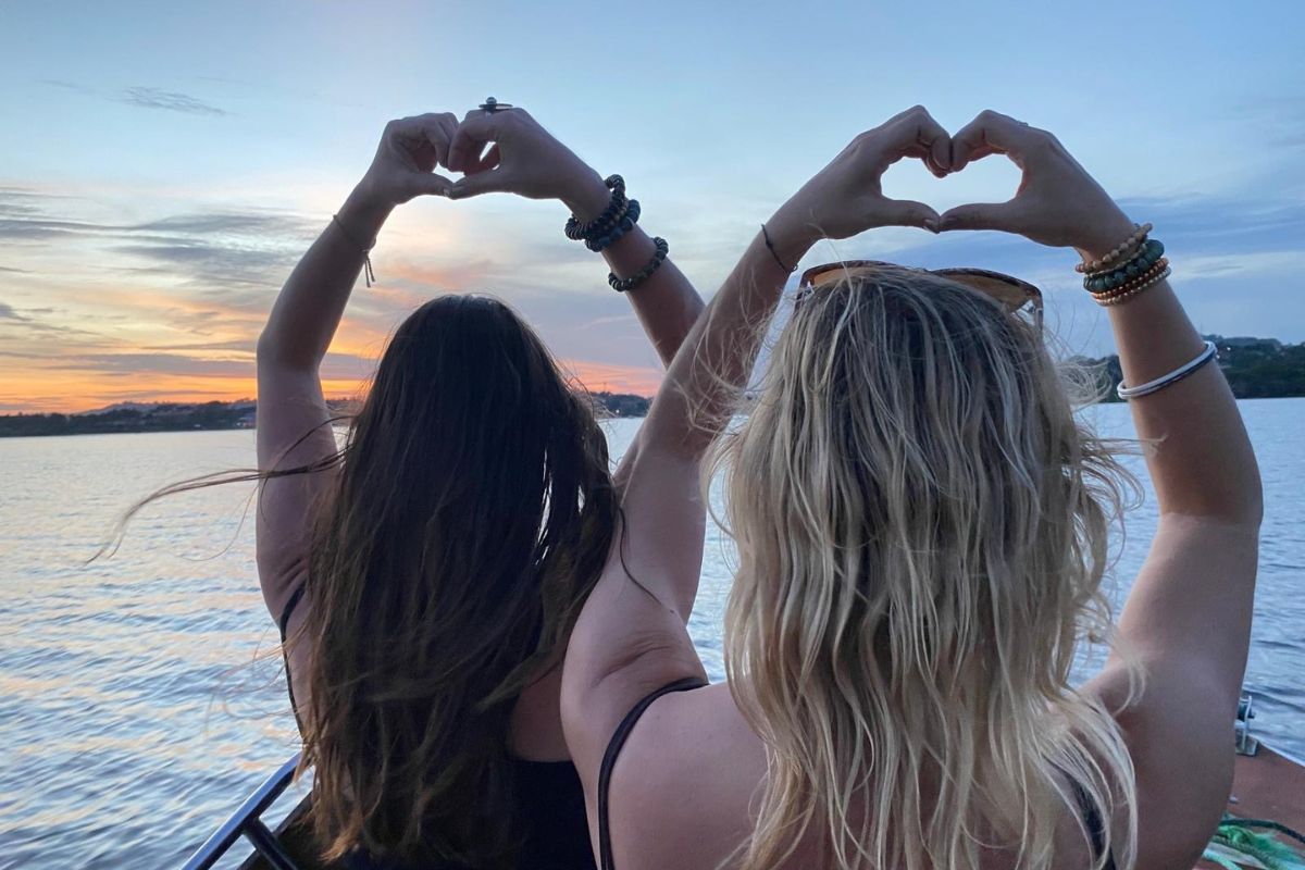 zwei Frauen formen ein Herz mit Ihren Händen auf einem boot während des Sonnenunterganges